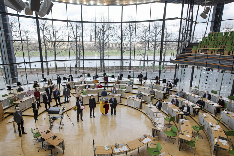 Mehrere Menschen sitzen in einem Plenarsaal.