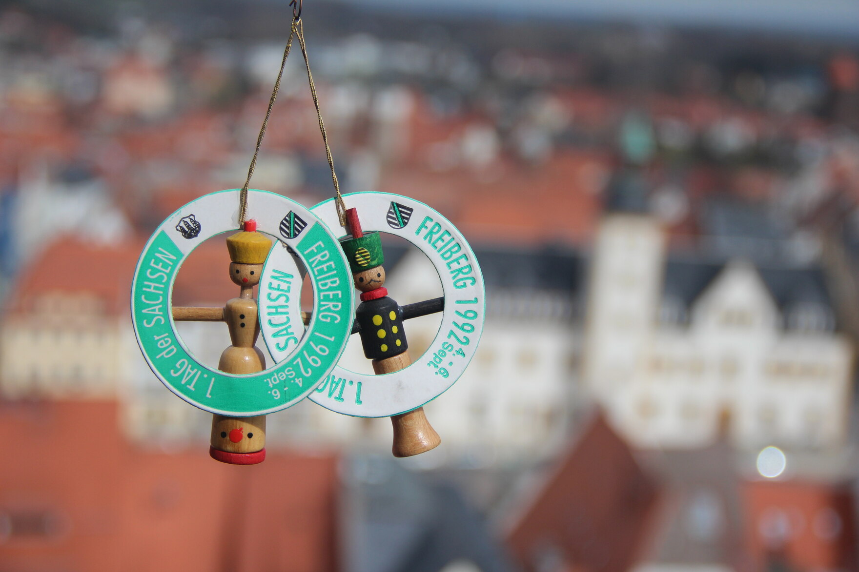 Zwei kleine Holzfiguren, die an grünen Anhängern hängen