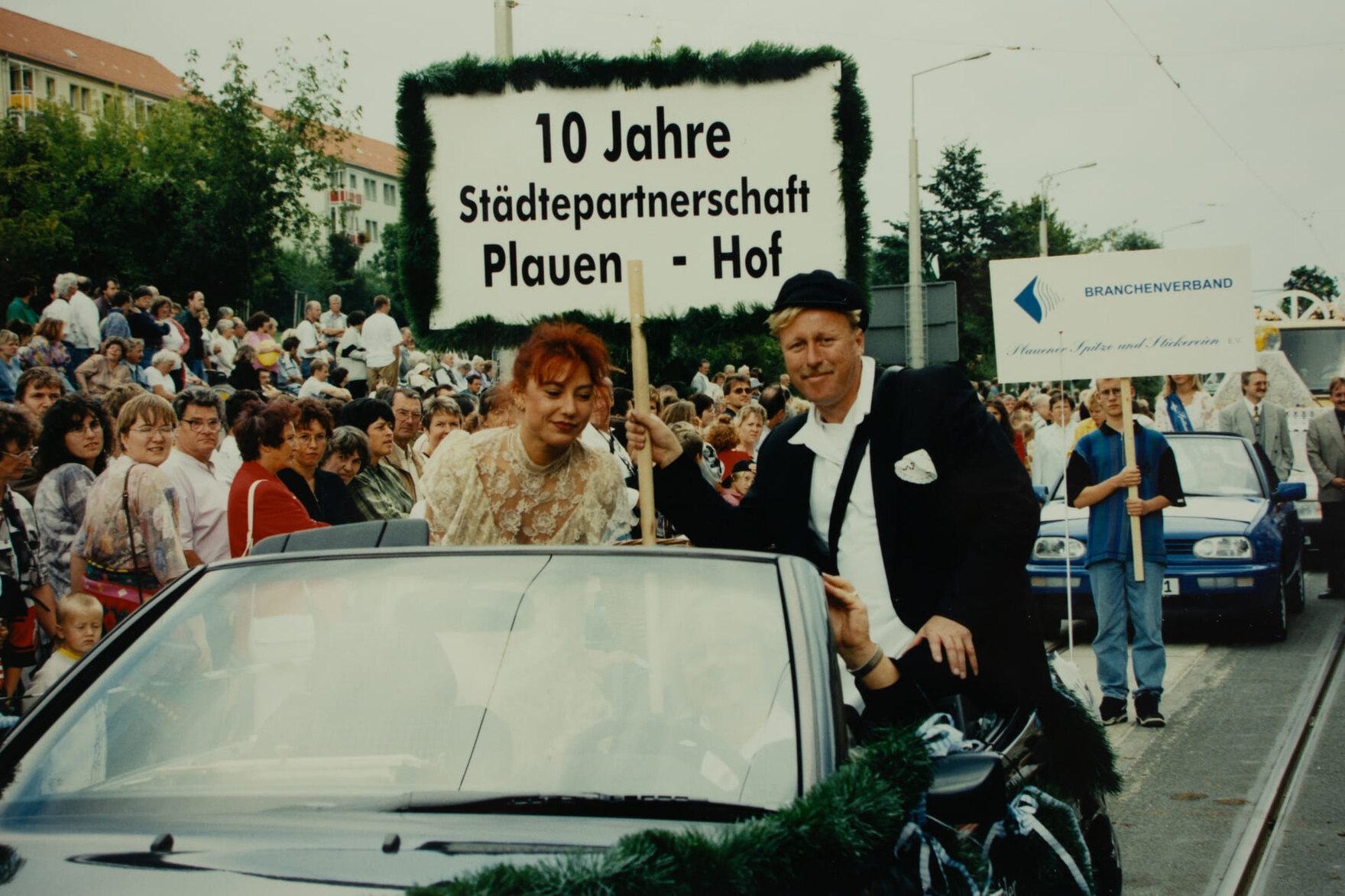 Ein festlich geschmücktes Cabrio mit zwei Personen und einem Schild mit der Aufschrift „10 Jahre Städtepartnerschaft Plauen – Hof“