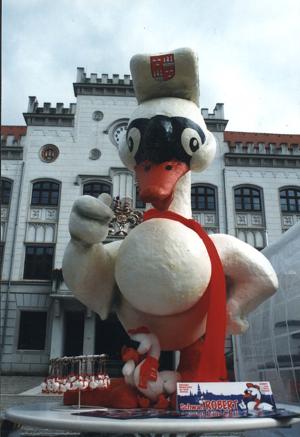 Übergroße Schwan-Figur mit rotem Schal vor einem alten Gebäude