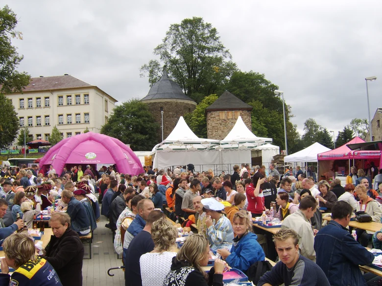 Viele Menschen sitzen an Biertischgarnituren im Freien, umgeben von bunten Pavillons