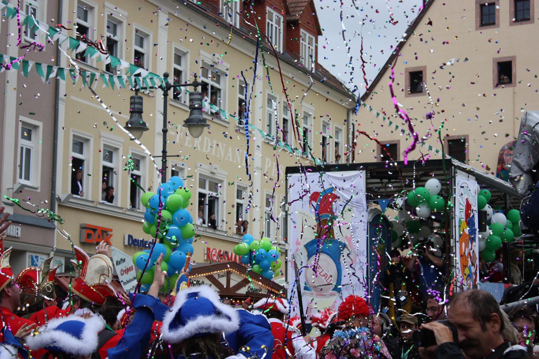 Menschen in bunten Kostümen feiern auf einer Straße mit Konfetti, Luftschlangen und Ballons