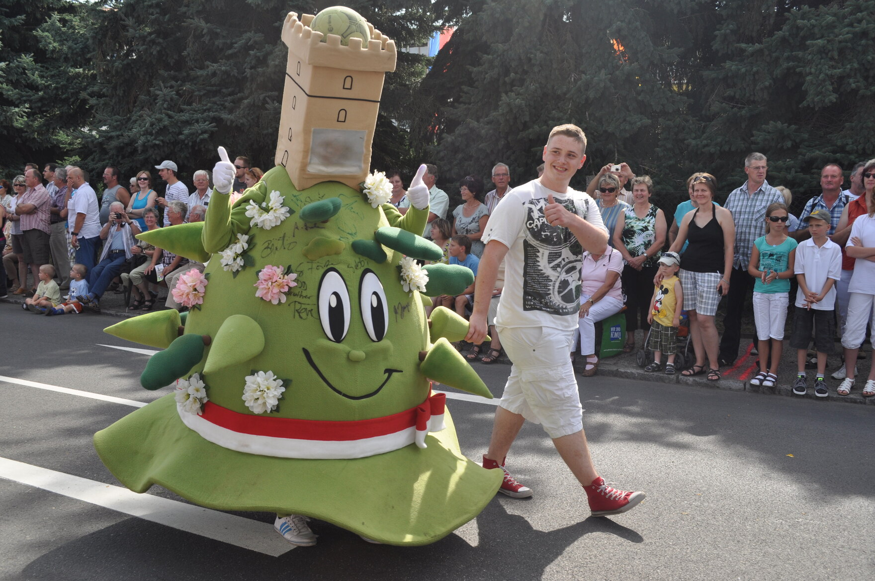 Eine Person in einem großen grünen Kostüm mit Blumen, einem lächelnden Gesicht und einem Turm auf dem Kopf