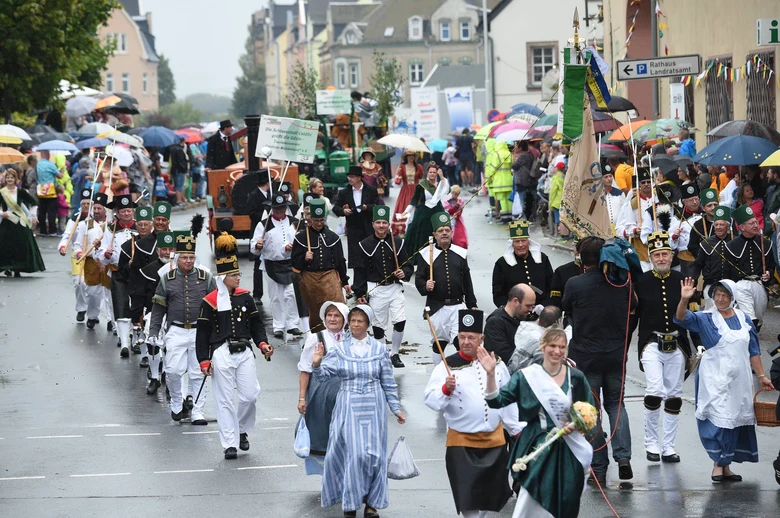 Menschen in historischen Bergmanns- und Festtagskostümen marschieren durch eine Straße, gesäumt von Zuschauern