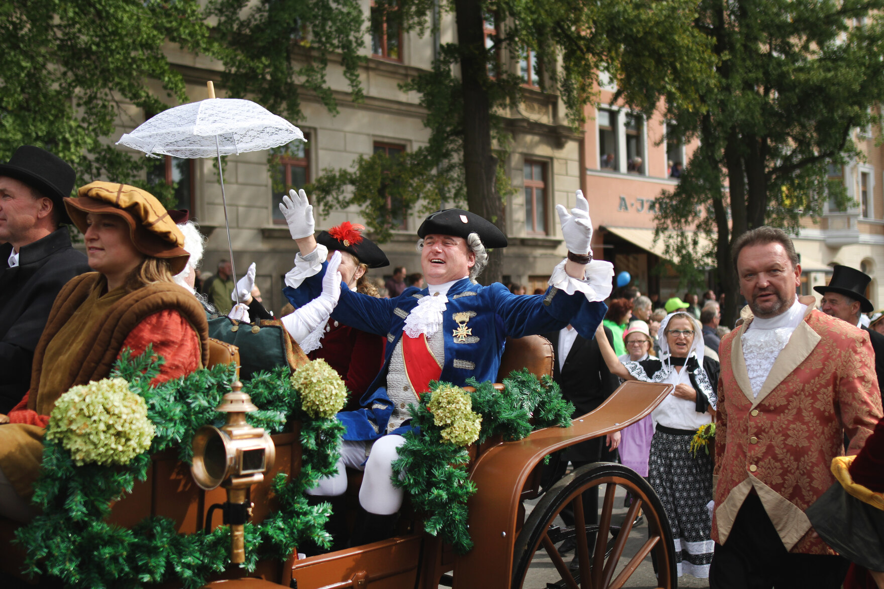 Menschen in historischen Kostümen fahren und gehen neben einer mit Blumen geschmückten Kutsche