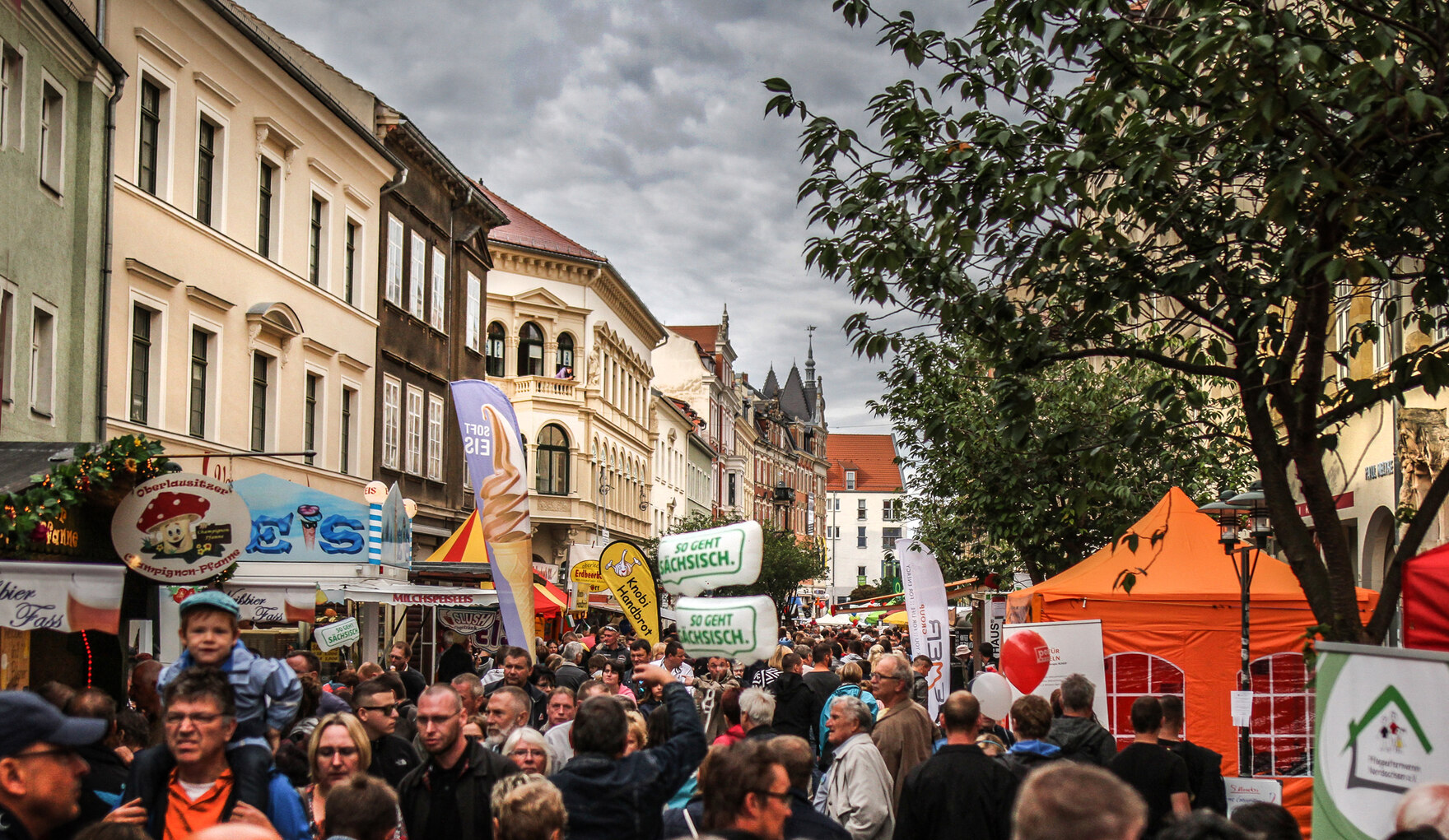 Menschenmenge in einer belebten Straße mit Marktständen und Pavillons