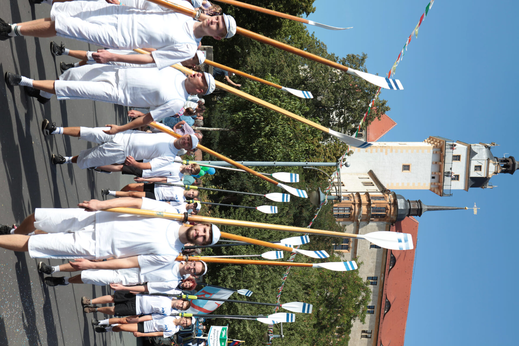 Eine Gruppe von Menschen in weißen Outfits mit Ruderblättern marschiert bei einer Parade
