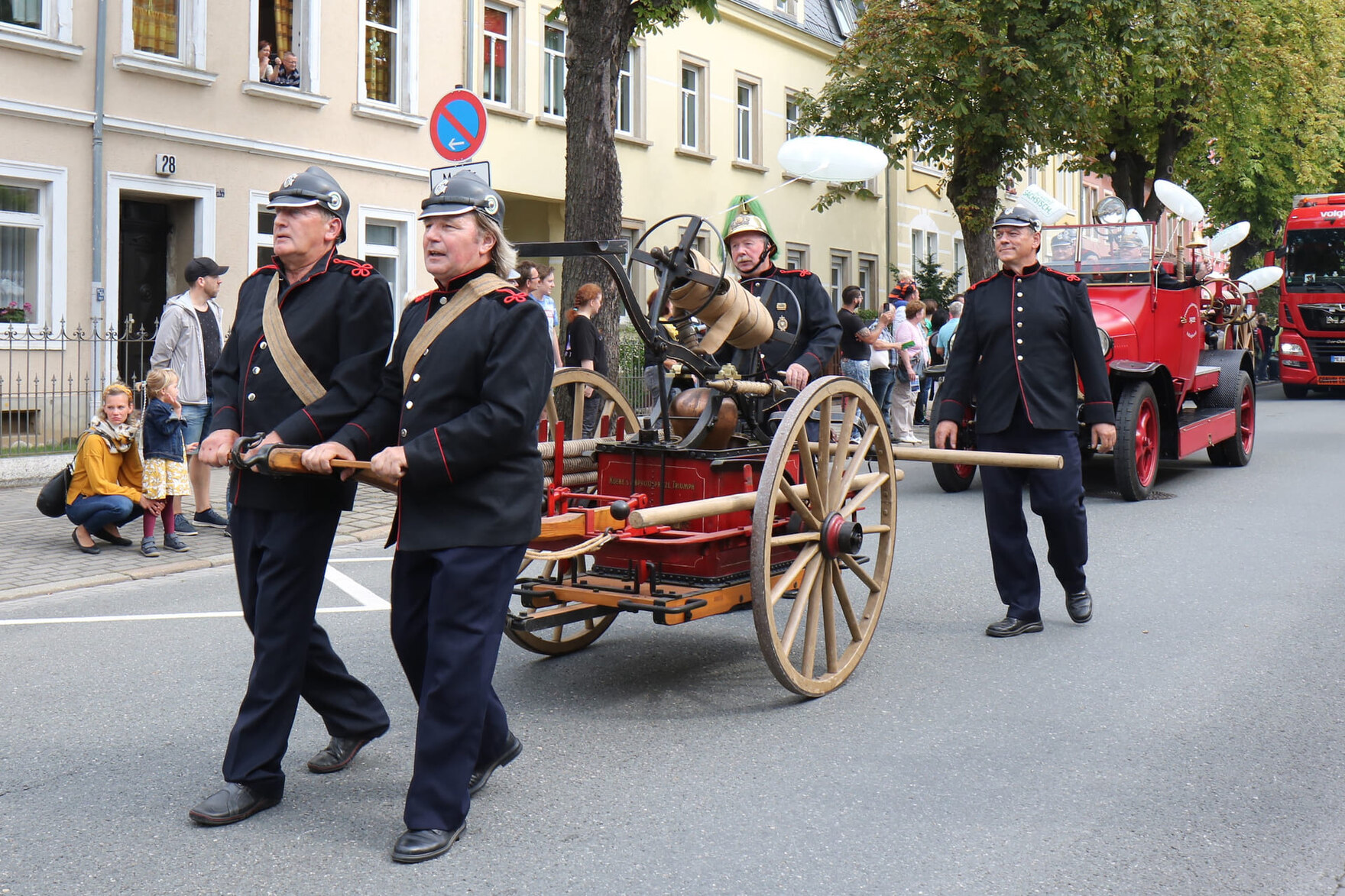 Mehrere Männer in historischen Feuerwehruniformen ziehen eine alte Handdruckspritze auf Rädern